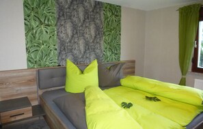 A bedroom with a bed, a nightstand, a wooden headboard, and a wall with a green leafy pattern.