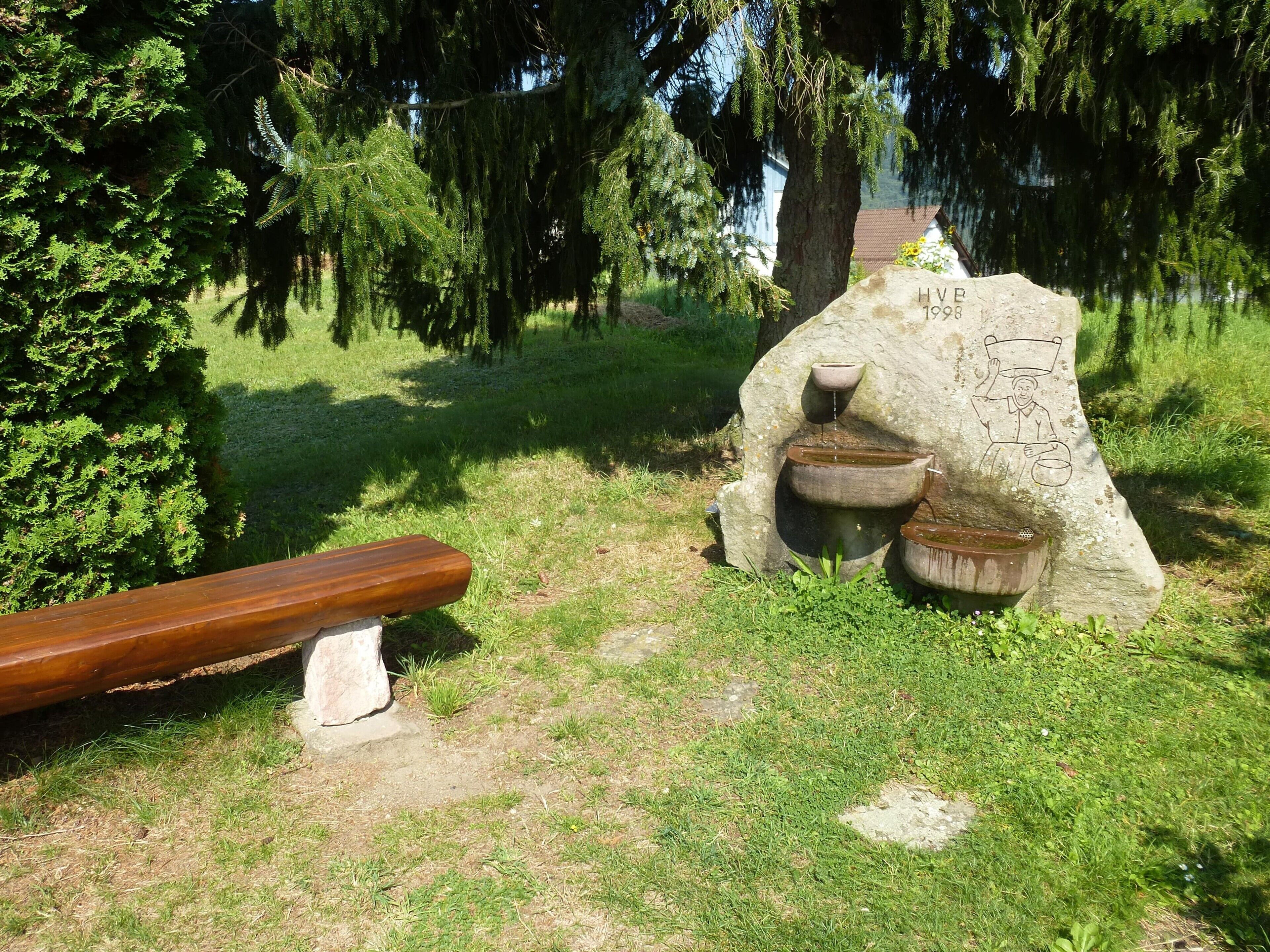 A stone structure with a carved figure, a bench, and a stone table.