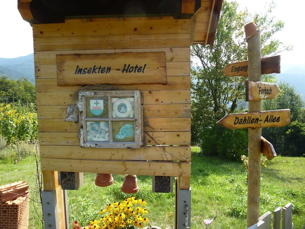 A wooden structure labeled 'Insekten - Hotel' with directional signs for 'Eingang' and 'Dahlen- Allee.'