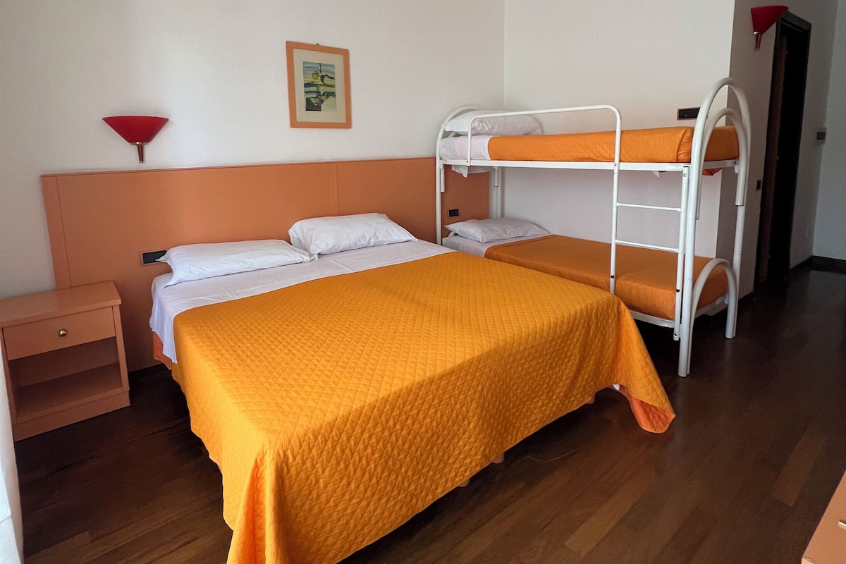 A room with a bunk bed, a single bed, a nightstand, and a wall-mounted lamp.