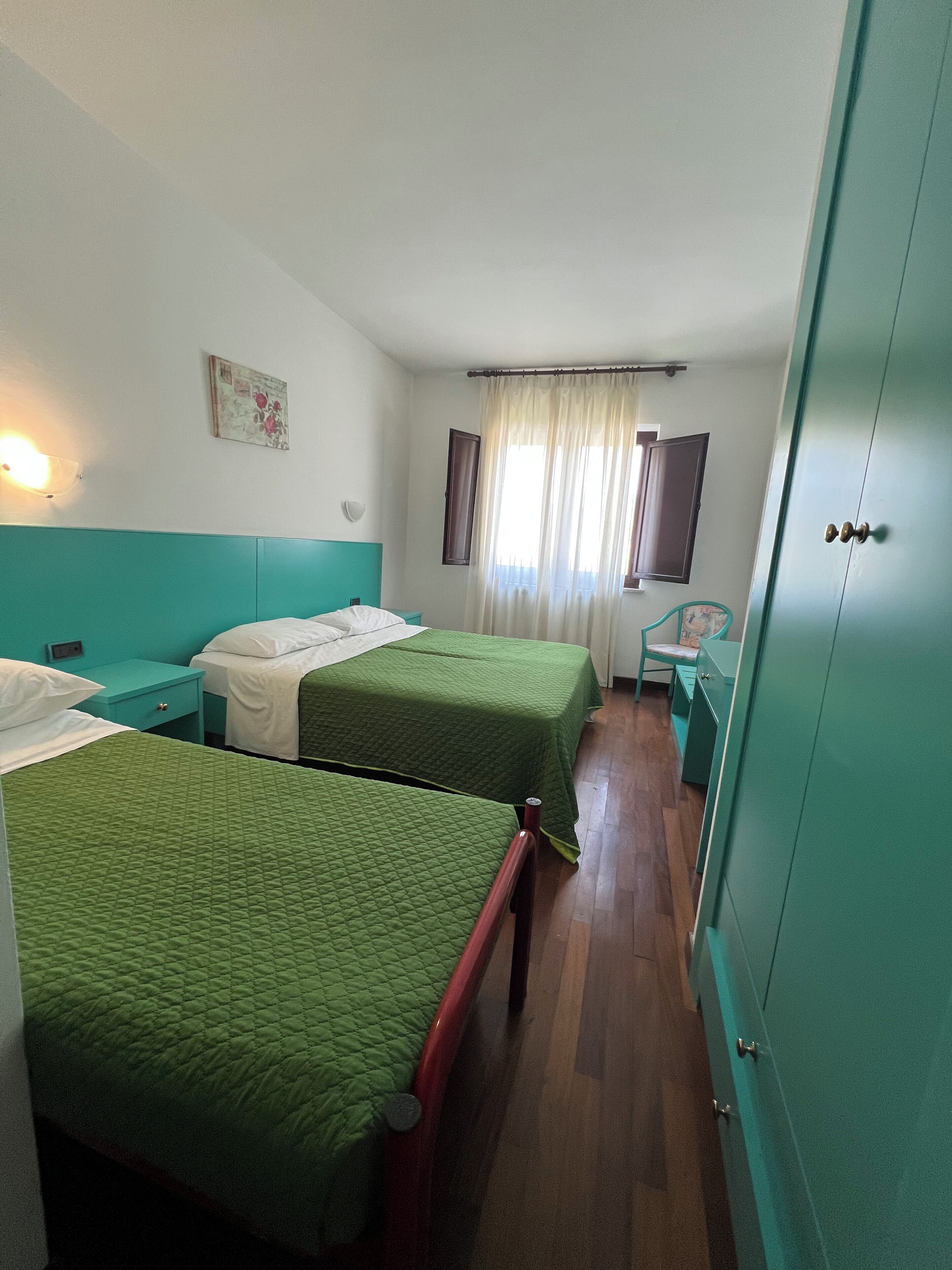 A room with two beds, a small table, a chair, and a wardrobe.
