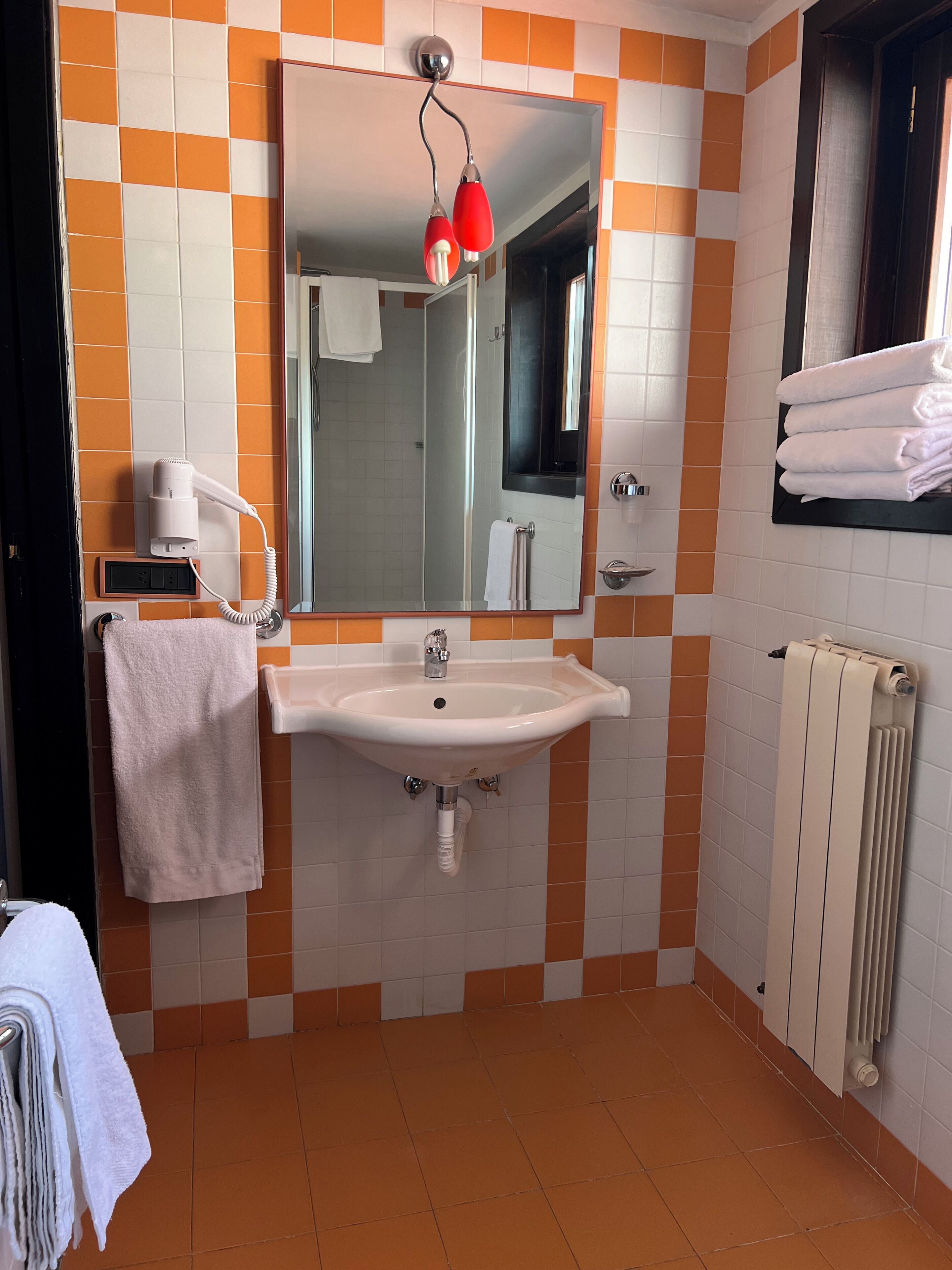 A bathroom with a sink, mirror, and orange and white tiled walls.