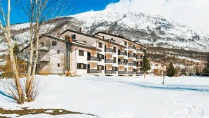 Ein mehrstöckiges Hotel mit Balkonen vor einer verschneiten Berglandschaft.