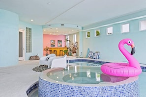 A swimming pool with a pink flamingo float, a seating area with white chairs, and a room with a pink wall and a window.