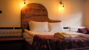 Ein Hotelzimmer mit einem Holzkopfteil, verziert mit Noten und dem Schriftzug "Piano Butik Oslo". Zwei Nachttischlampen, ein Bett mit weißen Leinen und eine violette Tagesdecke sind ebenfalls vorhanden.