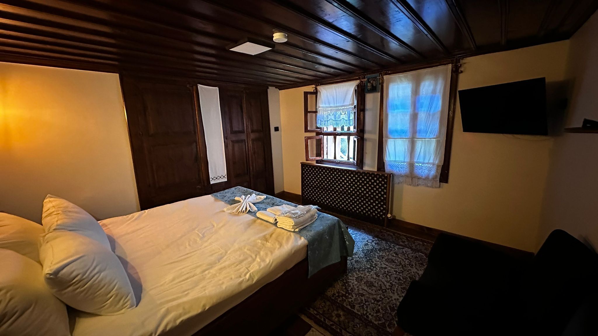 Ein Hotelzimmer mit Bett, Schreibtisch, Stuhl, einem Fenster mit Vorhängen und einem an der Wand montierten Fernseher.