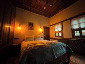 Een slaapkamer met een bed, nachtkastje, wandlamp, raam met kantgordijnen en een houten plafond.
