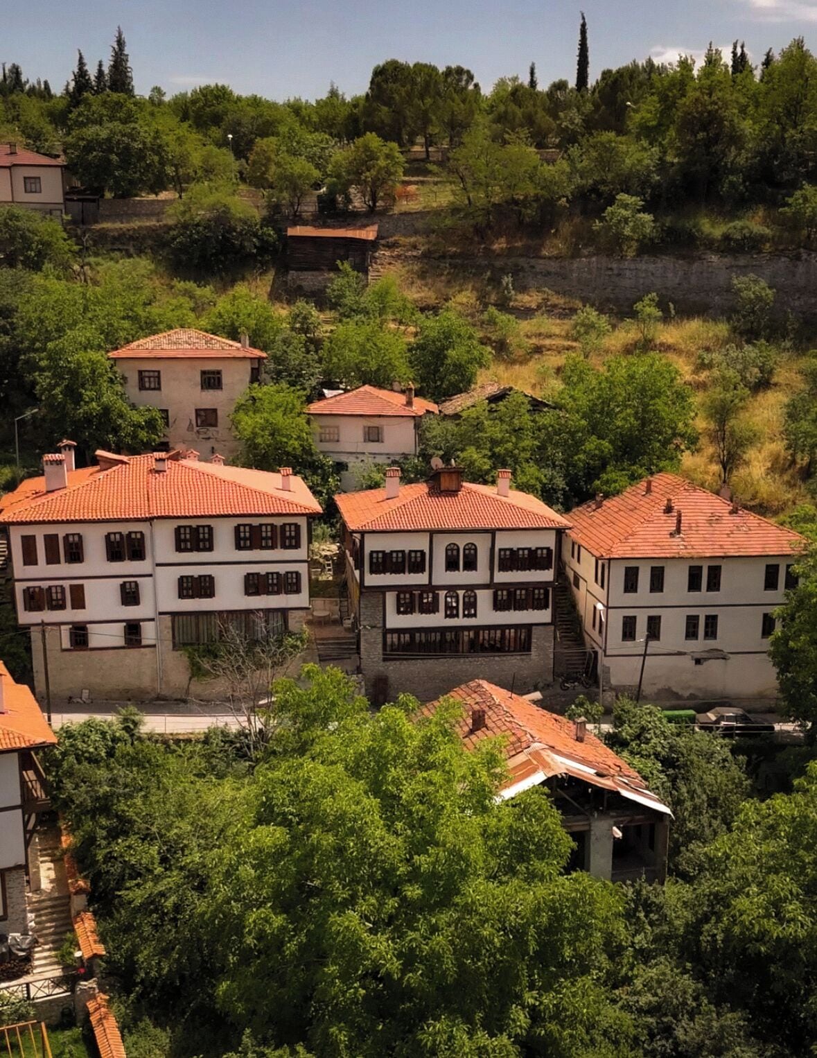 A cluster of traditional buildings with red-tiled roofs, surrounded by lush greenery and hills.