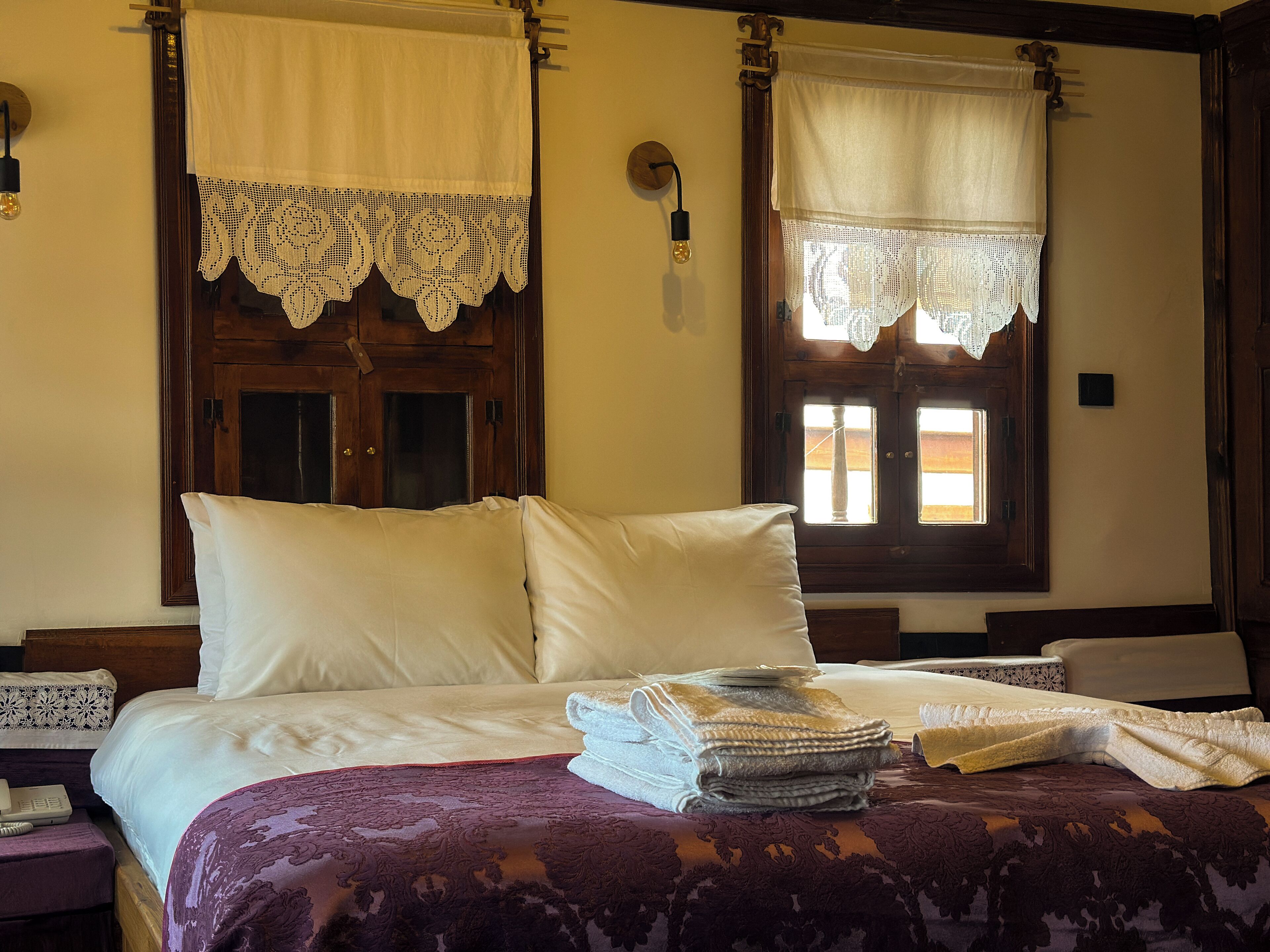 A room with a bed, a window with lace curtains, and a wooden door.