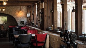 Un interno rustico con travi in legno, pareti in pietra e lampade d'epoca. Tavoli e sedie disposti per la sala da pranzo.