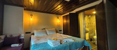 Habitación de hotel con una cama de madera, una mesita de noche, un sofá y un baño con ducha.