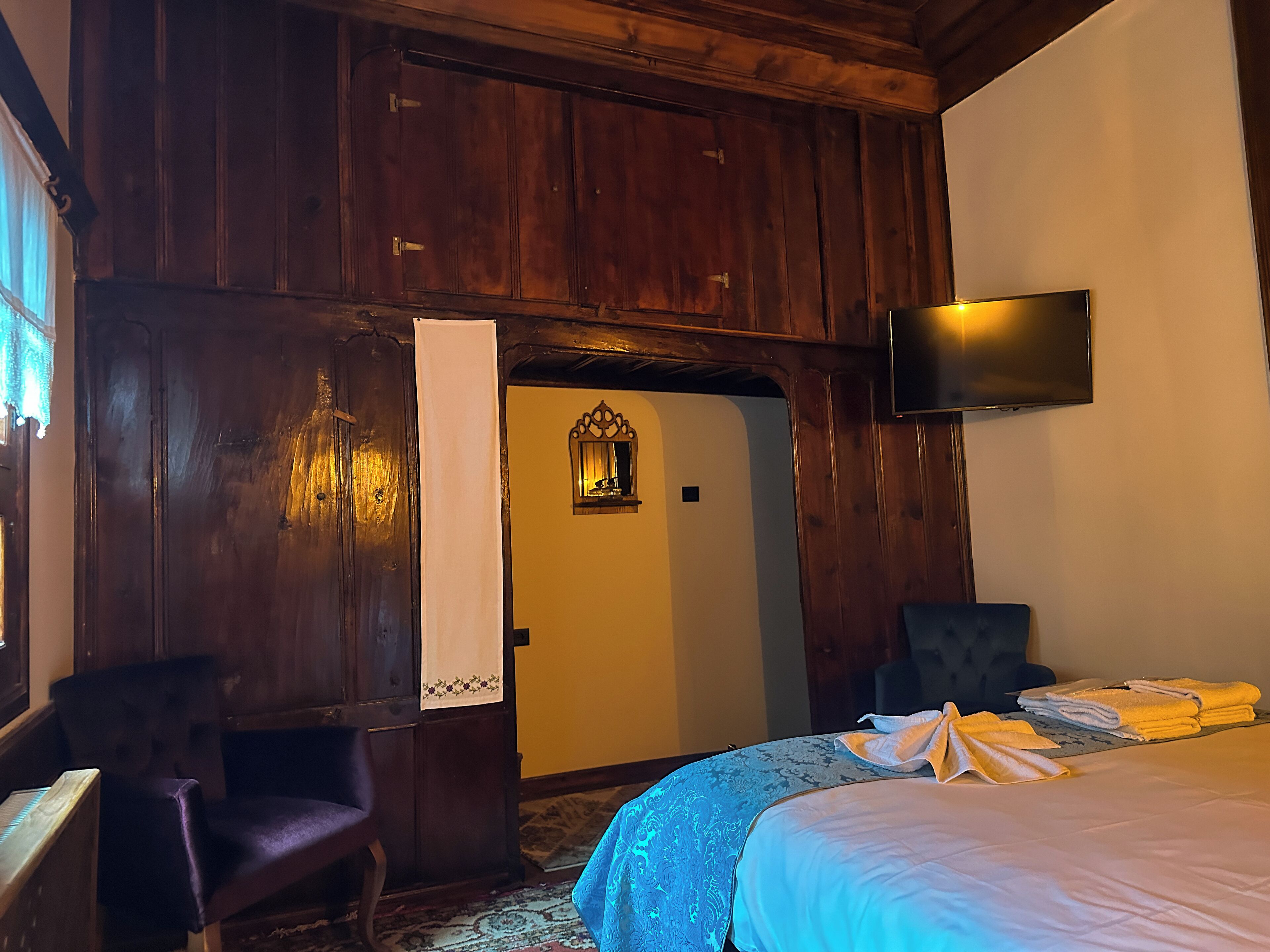 A room with wooden paneling, a bed with a blue bedspread, a chair, a flat-screen TV, and a door with a mirror.