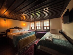 A room with two beds, wooden beams on the ceiling, and a window with lace curtains.