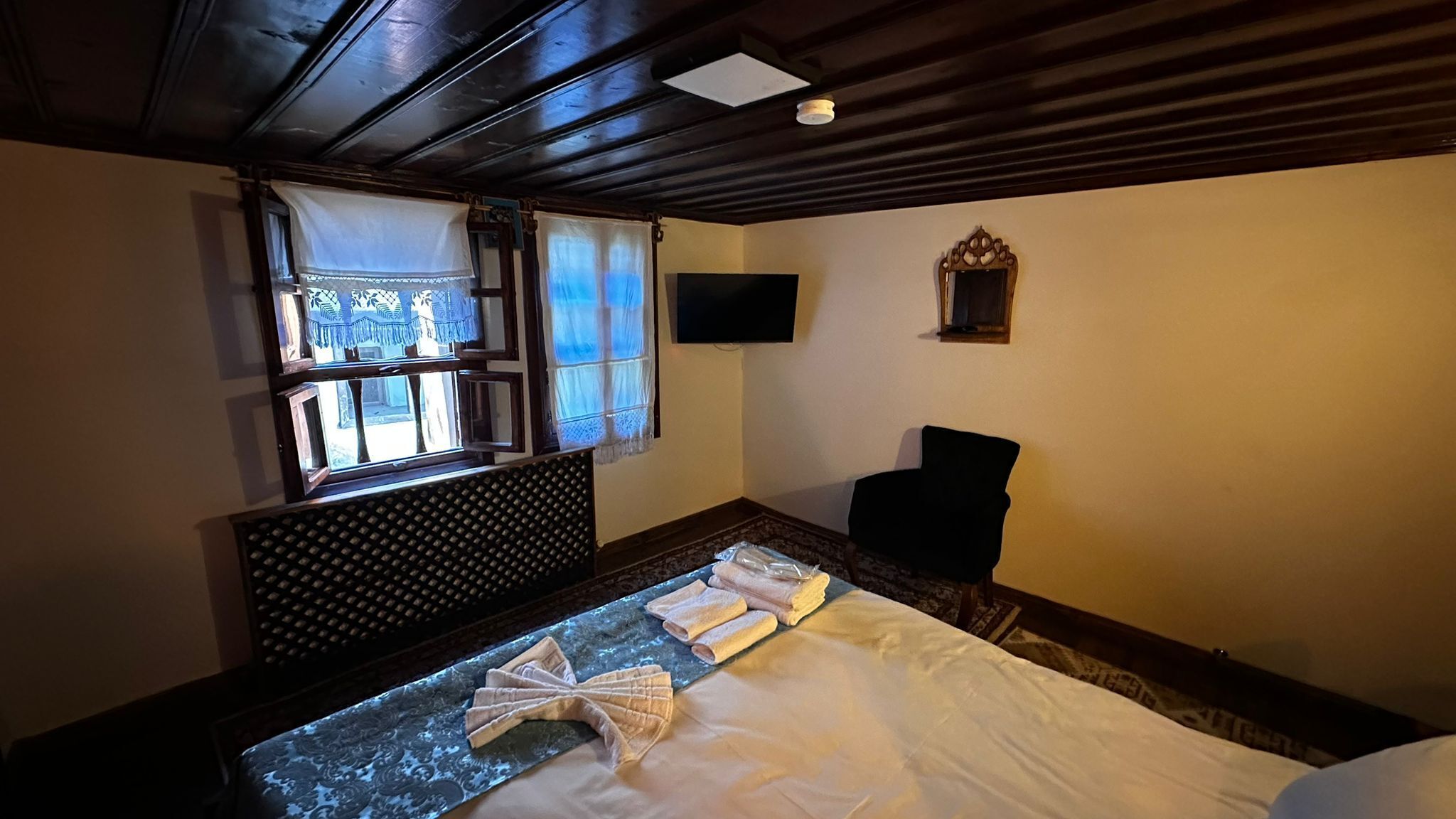 Habitación de hotel con cama, televisión montada en la pared y ventana con cortinas.
