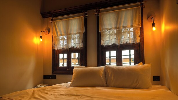 Una camera da letto con un letto, due finestre con tende, una lampada da comodino e un telefono sul comodino.
