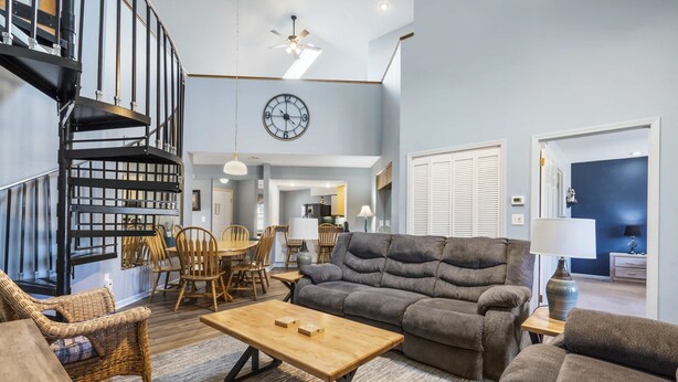 A spacious living area with a large gray sofa, a wooden coffee table, wicker chairs, and a spiral staircase. - Fairway Haven For 9! (Branson)