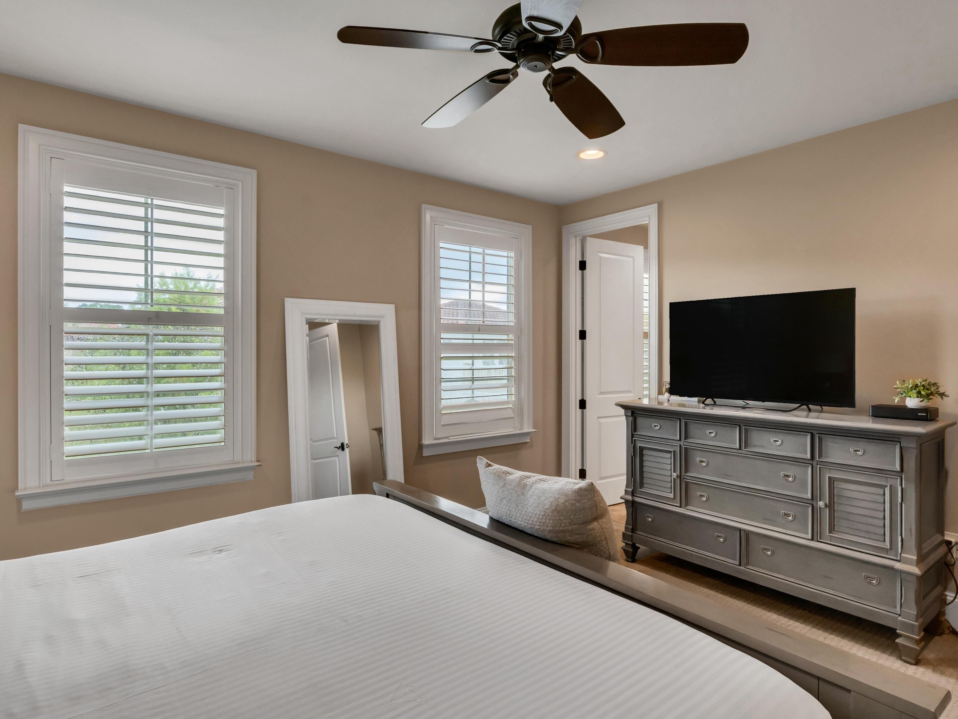 A bedroom with a bed, dresser, television, and ceiling fan.