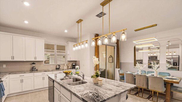 Une cuisine moderne avec des meubles blancs, un îlot en marbre et des luminaires suspendus.