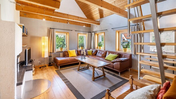 Ein geräumiges Wohnzimmer mit Holzbalkendecke, einer Sofagarnitur, einem Couchtisch und einem Fernseher.