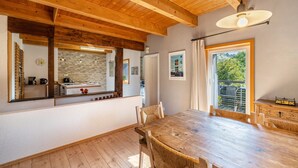 Ein Essbereich mit Holztisch und -stühlen, einer Steinwandverkleidung und einem großen Fenster mit Blick ins Grüne.