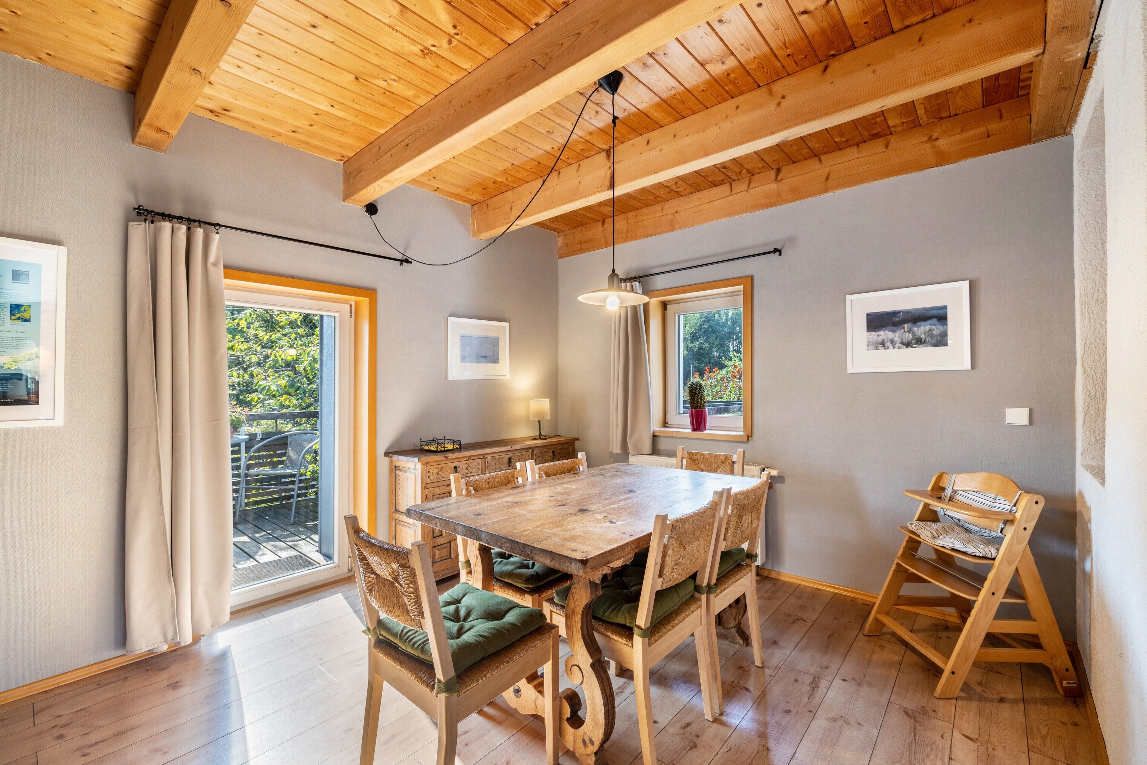 Un comedor con mesa y sillas de madera, una ventana con cortinas y un techo con vigas a la vista.