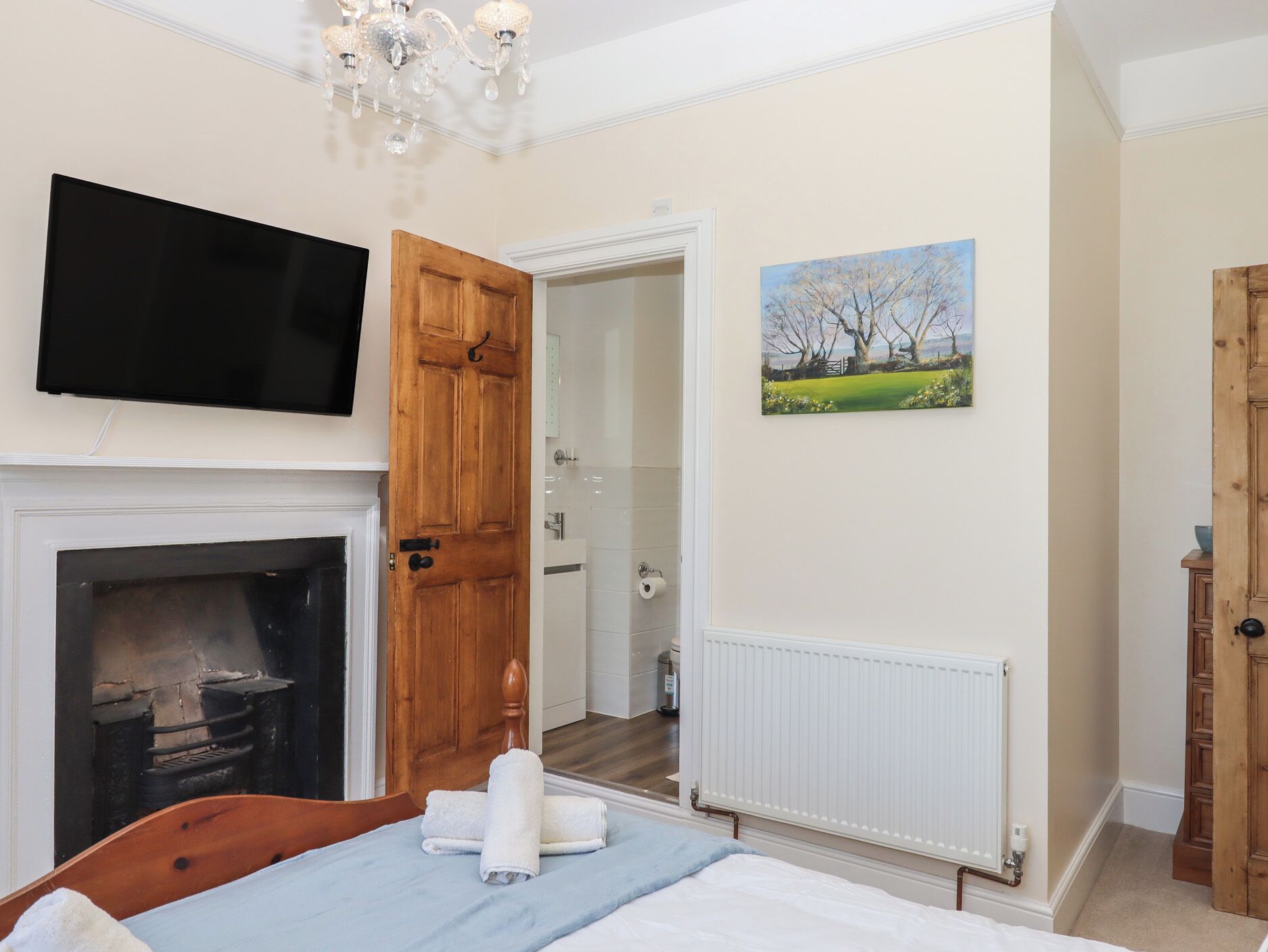 A bedroom with a fireplace, a television, a painting, and a door leading to a bathroom.
