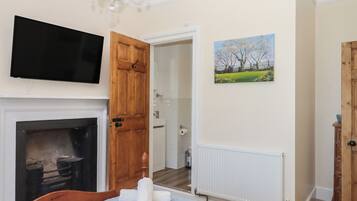 A bedroom with a fireplace, a television, a painting, and a door leading to a bathroom.