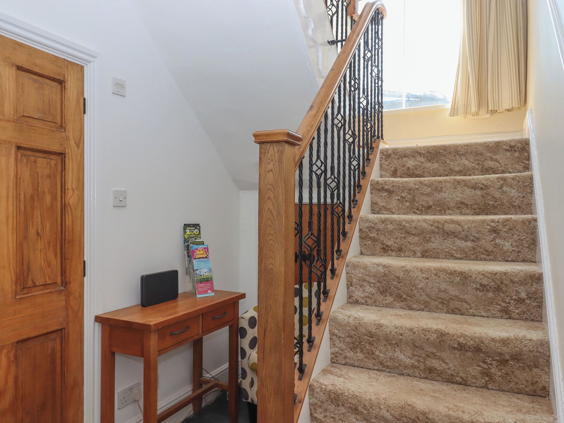 A staircase with wooden steps and a metal railing, a wooden door, and a small table with a box on it.