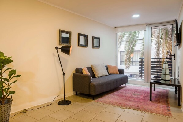 A living room with a grey sofa, a floor lamp, and a large window with a view of palm trees.