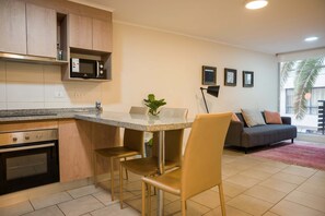 A modern kitchen with a built-in microwave, a dining area with a table and chairs, and a living room with a sofa and a plant. - Central 1BR1BA in Santiago Balcony & Nearby Metro (Unknown)