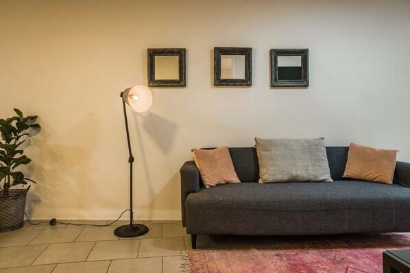 Un salon avec un canapé gris, deux coussins, une lampe sur pied et trois miroirs fixés au mur.