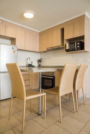 A modern kitchen with wooden cabinets, a white refrigerator, a microwave, and two chairs. - Metro-Accessible Apartment with Terrace Santiago (Santiago)