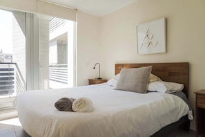 Un dormitorio con cama, mesita de noche, un cuadro en la pared y balcón.