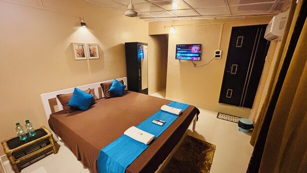 A hotel room with a large bed, a TV mounted on the wall, a wardrobe, and a small table with bottles.
