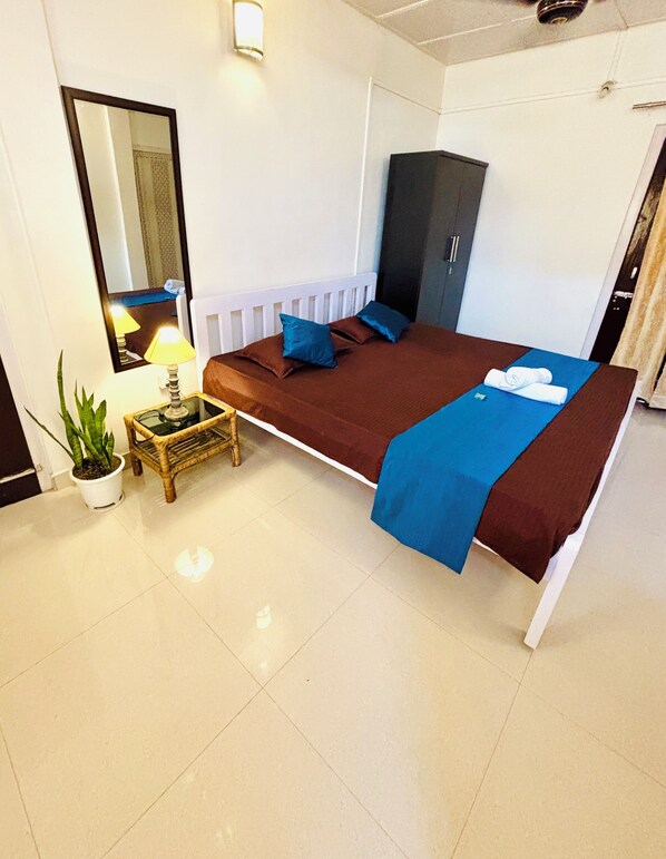 A hotel room with a bed, a nightstand, a potted plant, a mirror, and a wardrobe.