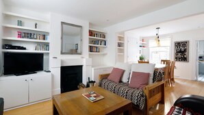 A modern living room with a flat-screen TV, bookshelves, a fireplace, a sofa with patterned cushions, and a dining area. - Superb 2 Bed Townhouse next to The Level Park (Brighton and Hove)