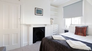 A modern bedroom with a fireplace, a bed with a dark headboard, a window with a view, and a white door. - Superb 2 Bed Townhouse next to The Level Park (Brighton and Hove)