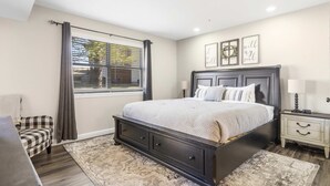 A bedroom with a large bed, a nightstand, a chair, and a window with curtains. - Fairway View Stay for 6! (Branson)