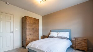 Een slaapkamer met een bed, een kledingkast, een nachtkastje en een dressoir.