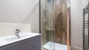 Een badkamer met een douche met glazen wand, een wit wastafelmeubel en een grijze kast.