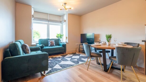A modern living room with a sofa, a dining table with chairs, a TV, and a large window. - Cartercroft Sheffield (Sheffield)