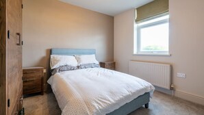 A bedroom with a bed, wooden wardrobe, bedside tables, a window, and a radiator. - Cartercroft Sheffield (Sheffield)