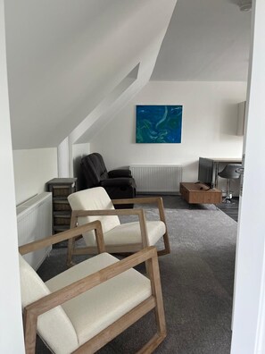 Uma sala de estar moderna com teto inclinado, um sofá de couro preto, uma mesa de centro de madeira e um quadro abstrato azul na parede.