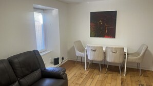 A room with a leather sofa, a dining table with four chairs, and a painting on the wall.