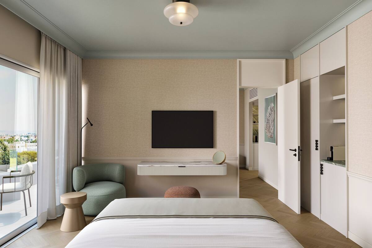 Quarto moderno com cama, uma cadeira verde, mesa de cabeceira, janela ampla e vista da cidade.