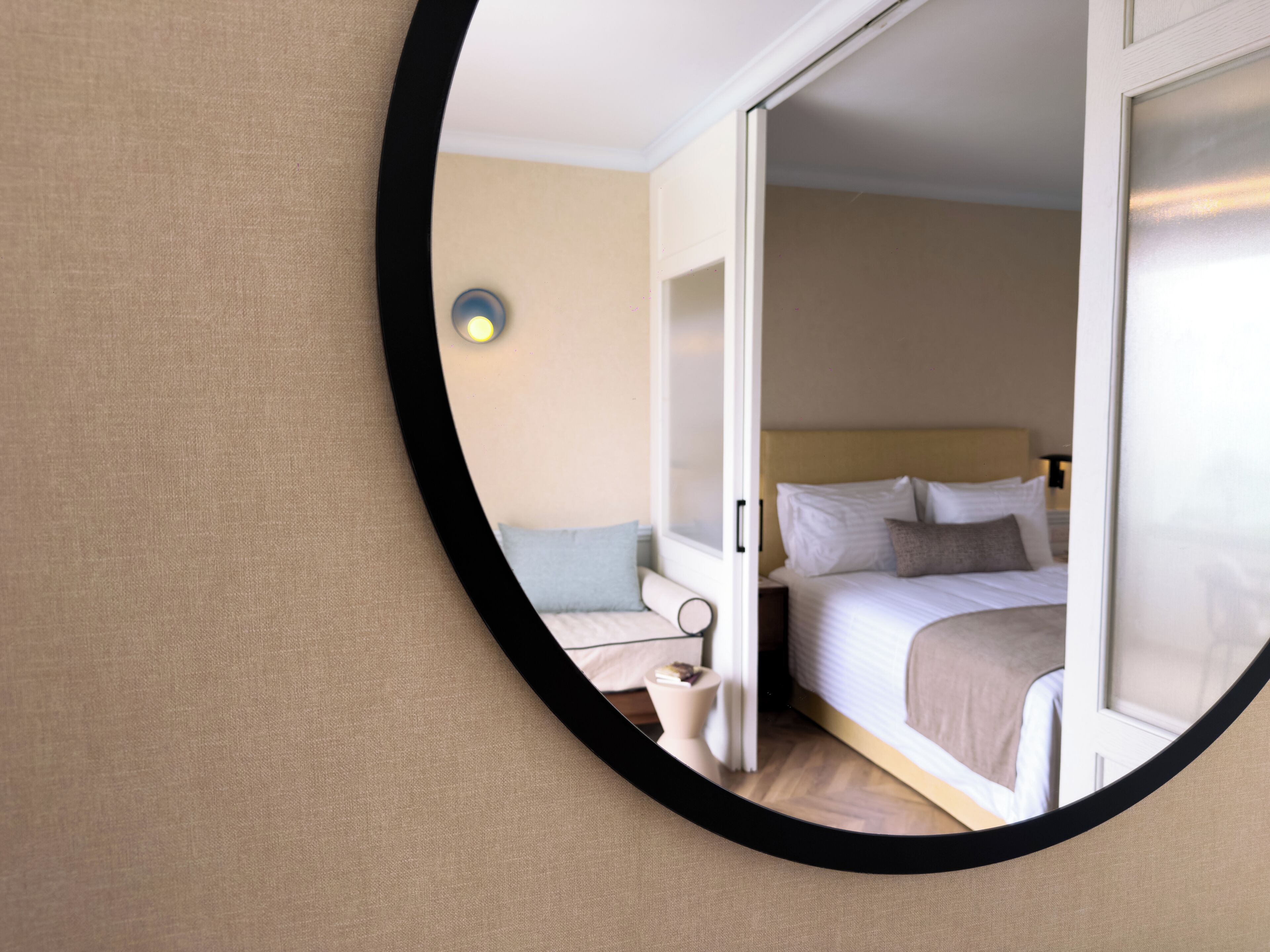 A hotel room with a bed, bedside table, and a mirror reflecting the room.
