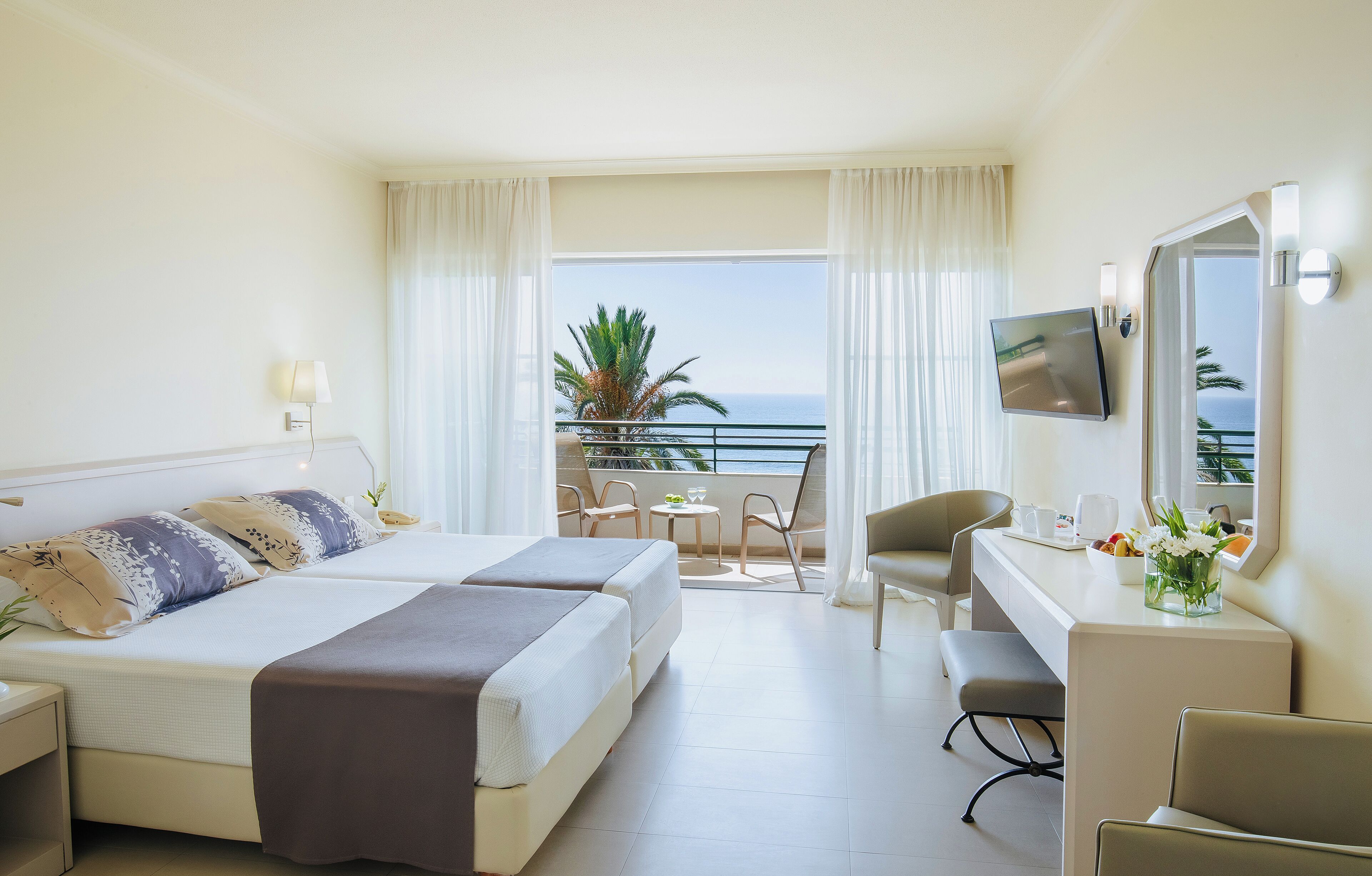 Ein Hotelzimmer mit Bett, Schreibtisch, Stuhl und einem Balkon mit Meerblick.