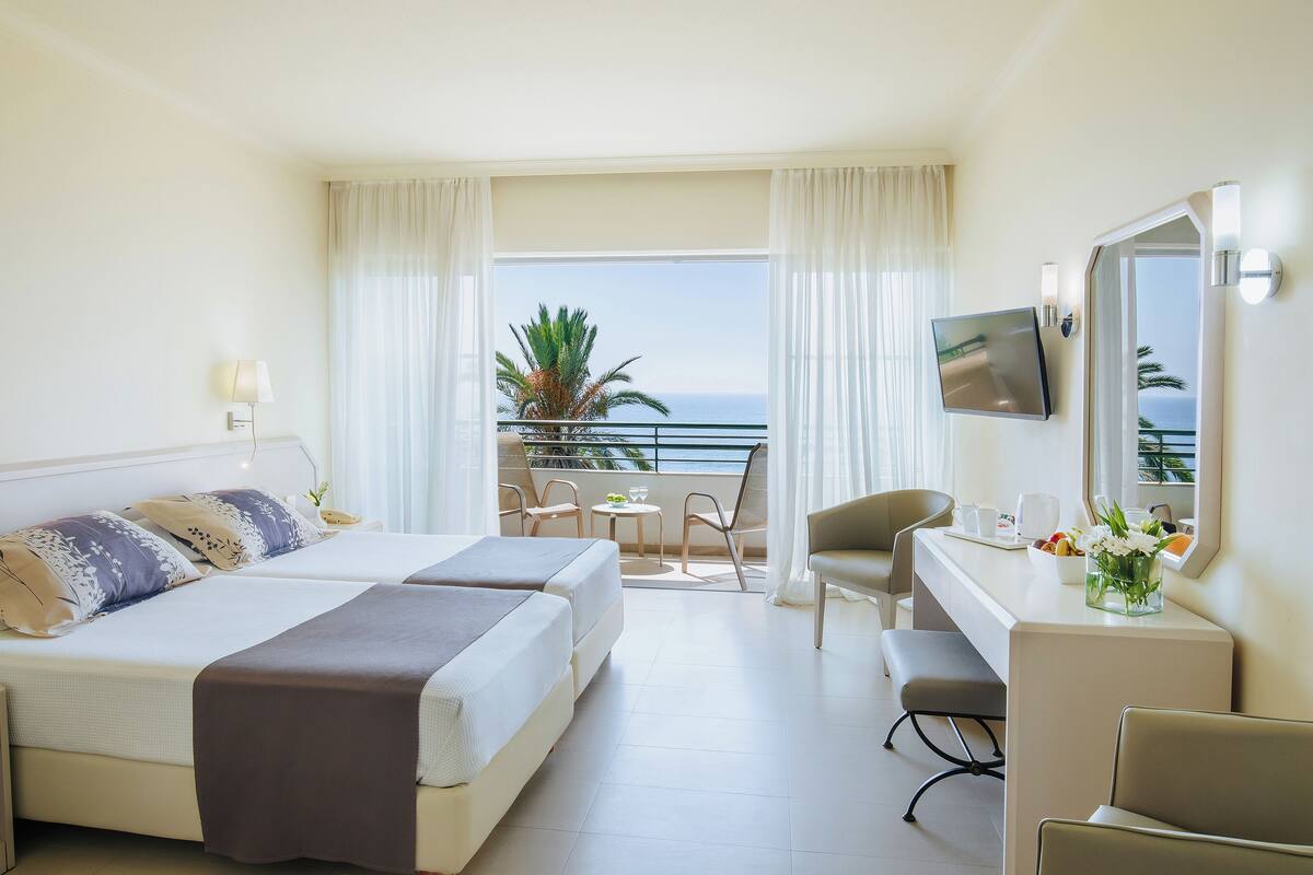 Ein Hotelzimmer mit Bett, Schreibtisch, Stuhl und einem Balkon mit Meerblick.