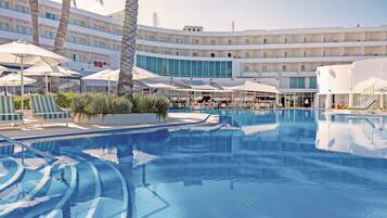 A hotel pool area with multiple levels of balconies, sun umbrellas, and lounge chairs.