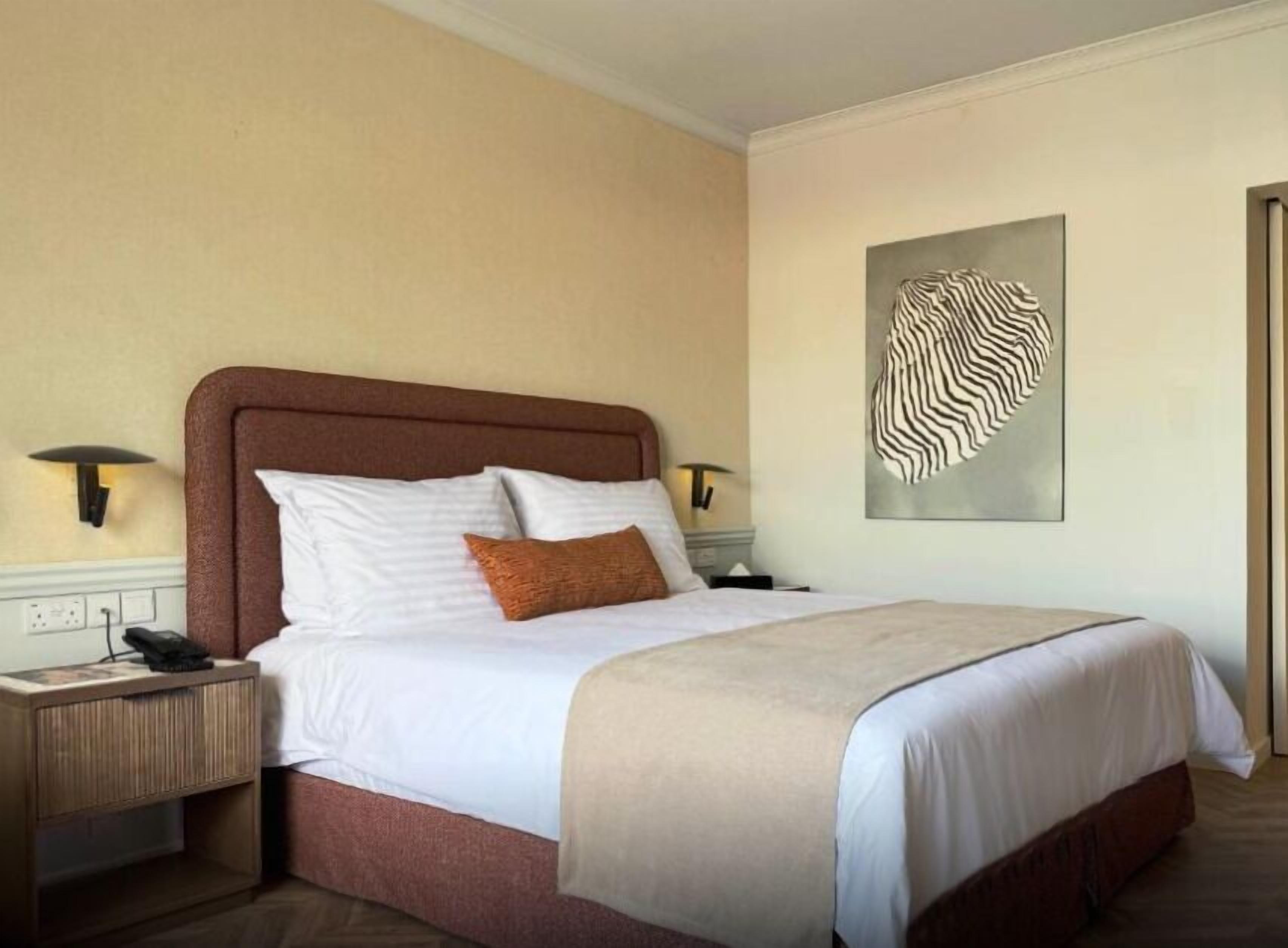 Ein Hotelzimmer mit einem Bett, Nachttischen, einem Wandbild und einer Tür.